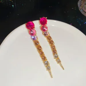 Detailed view of elegant gradient pink and amber rhinestone tassel earrings on a white tray.