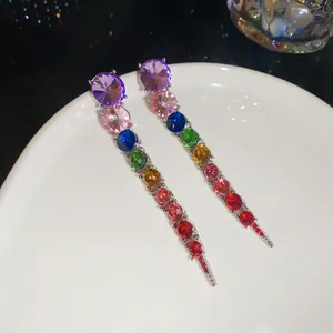 Detailed close-up of rainbow gradient crystal tassel earrings resting on a white ceramic plate.