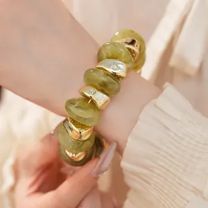 Gedetailleerde weergave van een elastische armband met olijfgroene en gouden kralen om de pols.