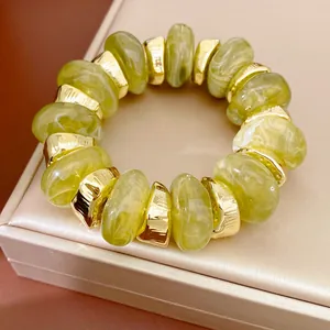 Detailopname van groene marmeren acrylkralen en goudkleurige kralen op een elastische armband.