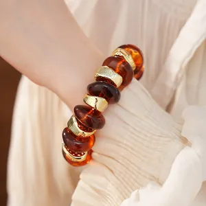 Macro detail van amberkleurige acrylkralen en gouden afstandskralen op elastische armband
