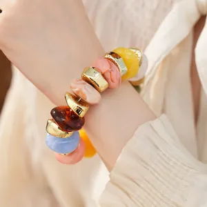 Close-up van een kleurrijke acryl elastische armband met gouden kralen gedragen om de pols.