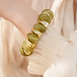Detailweergave van groene acryl en goudkleurige kralenarmband op de pols van model