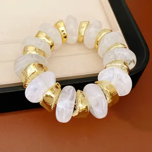 Detailopname van gemarmerde witte acryl en gouden geometrische kralen op een elastische armband