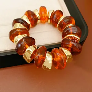 Close-up van barnsteen kralen en onregelmatige gouden stukjes op een elastische armband.