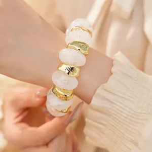 Detail van een elastische armband met witte acryl- en goudkleurige geometrische kralen