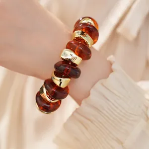 Detailopname van een elastische armband met amberkleurige acryl en gouden kralen