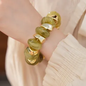 Detailopname van een elastische armband met olijfgroene acryl en gouden metalen kralen