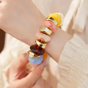 Detailopname van een elastische armband met kleurrijke acryl- en goudkleurige kralen