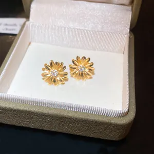 Primer plano detallado de pendientes de margarita dorados con circón en un estuche de joyas