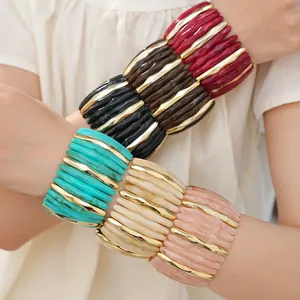 Stack of colorful acrylic marbled bracelets with gold accents worn on female arms