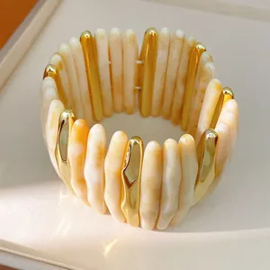 Close-up detail of marbled cream acrylic and gold-tone segmented elastic bracelet cuff