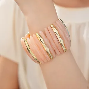 Close-up detail of marbled pink acrylic and gold-toned metal elastic bracelet on woman's wrist.