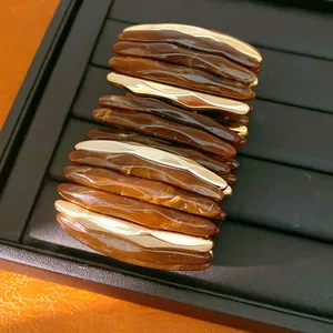 Detail shot of acrylic marbled stretch bracelet with gold metal accents on a black tray.
