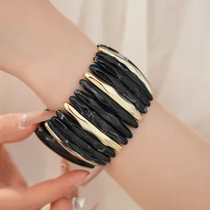 Close-up detail of a marbled black and gold leaf-shaped acrylic elastic bracelet on wrist
