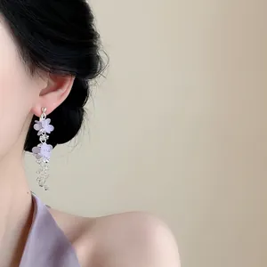 Detailopname van elegante zilveren oorhangers met paarse bloemen hangers op een model.