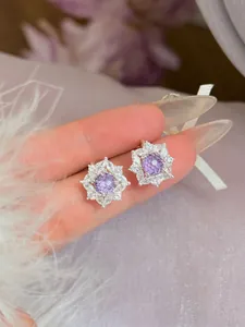 Detailopname van elegante bloemvormige oorknopjes met paarse zirkoon en zilveren naald
