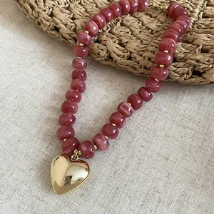 Dettaglio di perle acriliche rosa marmorizzate con un ciondolo a cuore dorato lucido.