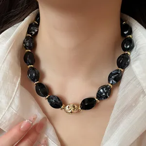 Close-up of a stylish choker with black marble acrylic beads and a gold twisted central knot.