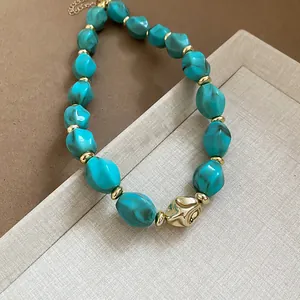 Detail shot of turquoise acrylic twisted beads with golden spacers on a necklace.