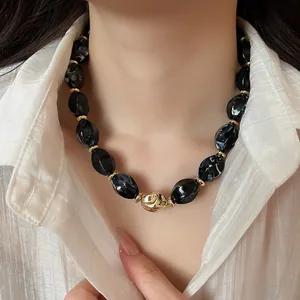 Close-up of black marble acrylic oval bead necklace with gold accents on model
