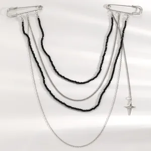 Dettaglio della spilla a catena multistrato con spille da balia e perline nere.