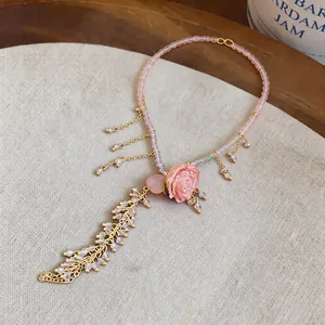 Detailed macro shot of a pink floral pendant necklace featuring golden feather charms