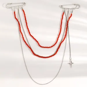 Dettaglio di spilla a nappe multistrato con perle rosse, catene argentate e ciondolo stella.