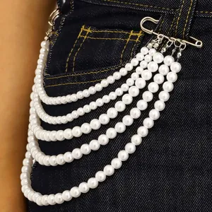 Detalle de accesorio de cadena de perlas multicapa fijado en unos vaqueros oscuros.