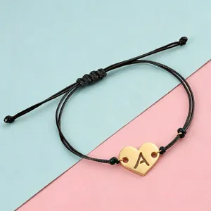 Detail of adjustable black cord bracelet with gold heart charm and cut-out letter A