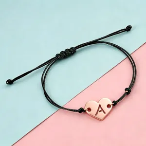 Close-up of rose gold heart charm with hollowed letter A on braided bracelet