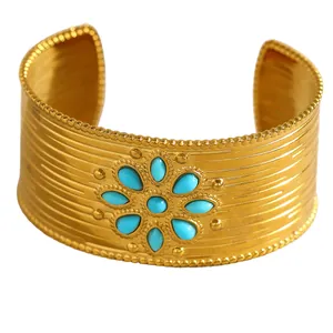 Détail d'un large bracelet manchette en acier doré avec motif fleur en turquoise bleue