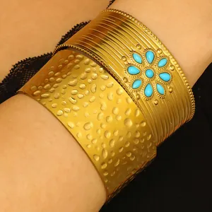 Détail d'une manchette large dorée avec motif fleur turquoise et texture martelée