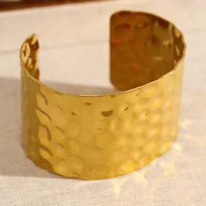 Détail macro de la texture martelée sur un bracelet manchette large doré en inox.