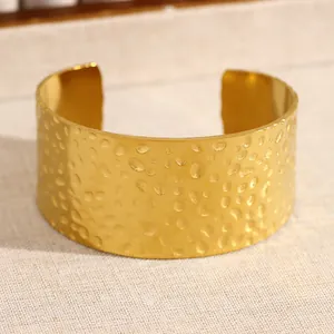 Gros plan d'un large bracelet manchette doré en acier inoxydable à texture martelée.