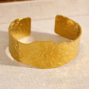 Gros plan d'un bracelet manchette en acier doré avec texture martelée et bords ondulés