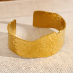 Gros plan sur un bracelet manchette doré large avec texture martelée et bords ondulés