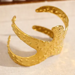 Gros plan d'un large bracelet doré avec une texture martelée et un design ondulé ouvert
