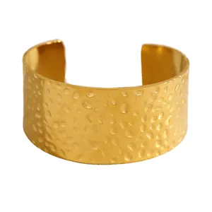 Vue détaillée d'un large bracelet manchette doré en acier inoxydable avec texture martelée.
