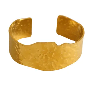 Gros plan sur la texture martelée et les bords ondulés de ce large bracelet manchette doré