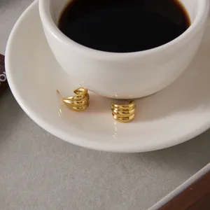 Detailed view of chunky gold C-shaped earrings on a white coffee saucer.