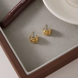 Close-up of golden C-shaped hoop earrings with multi-layer ribbed texture