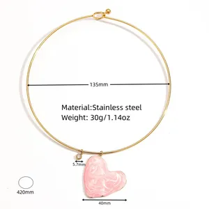 Détail en gros plan du pendentif cœur marbré rose et du collier ras de cou en acier doré