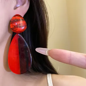 Detailansicht großer rot-maronbraun marmorierter Harz-Tropfenohrringe am Ohr eines Models