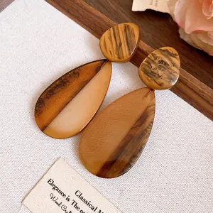Detailansicht brauner Marmor-Resin-Tropfenohrringe auf rustikalem hellem Stoffhintergrund.