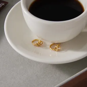 Detail view of gold zirconia multi-hoop titanium steel earrings on a coffee saucer
