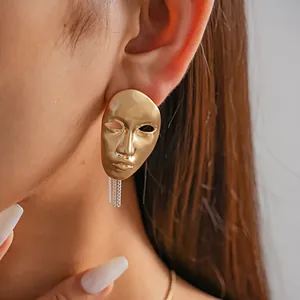Close-up of a bold gold artistic human face mask earring with chain tassel detail