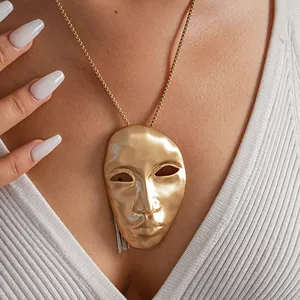 Close-up detail view of an avant-garde gold mask pendant necklace worn on a model's neck.