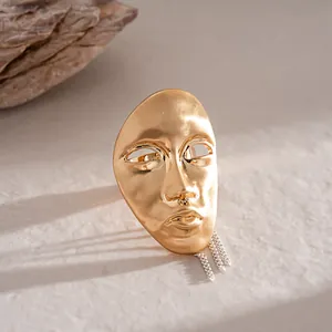 High-detail macro shot of a golden artistic portrait mask pendant with silver chains.