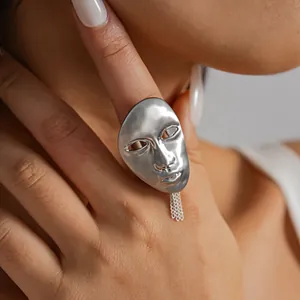 Close-up detail of a silver metal portrait mask ring featuring a dangling chain on the hand